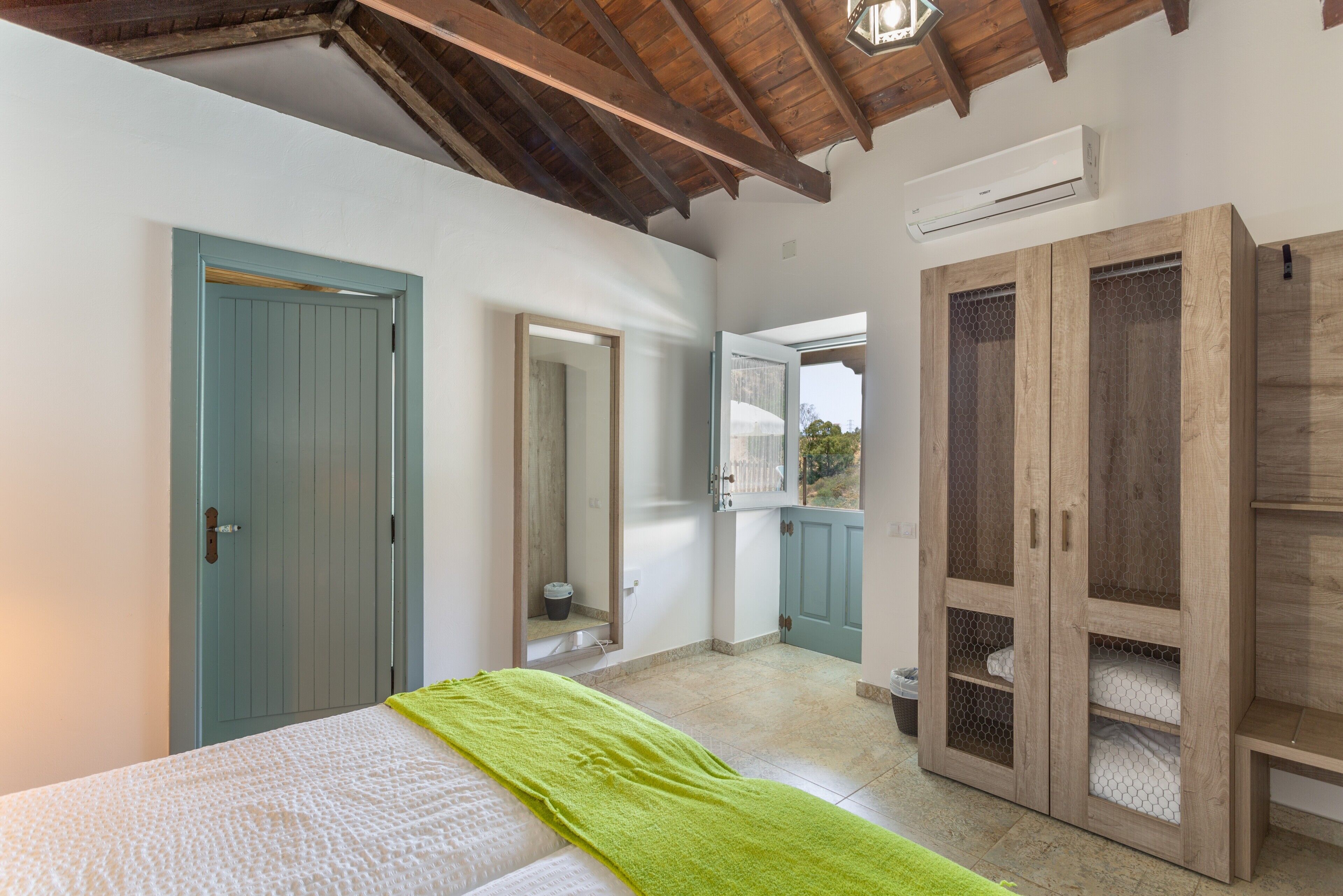 A bedroom with a bed, a green towel, a wardrobe, and an air conditioning unit.