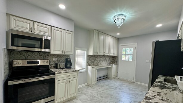 A kitchen with white cabinets, stainless steel appliances, a marble countertop, and a chandelier. - Cozy Upper-Level Retreat (Waukegan)