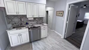 A modern kitchen with white cabinetry, a stainless steel dishwasher, and a marble countertop. - Cozy Upper-Level Retreat (Waukegan)