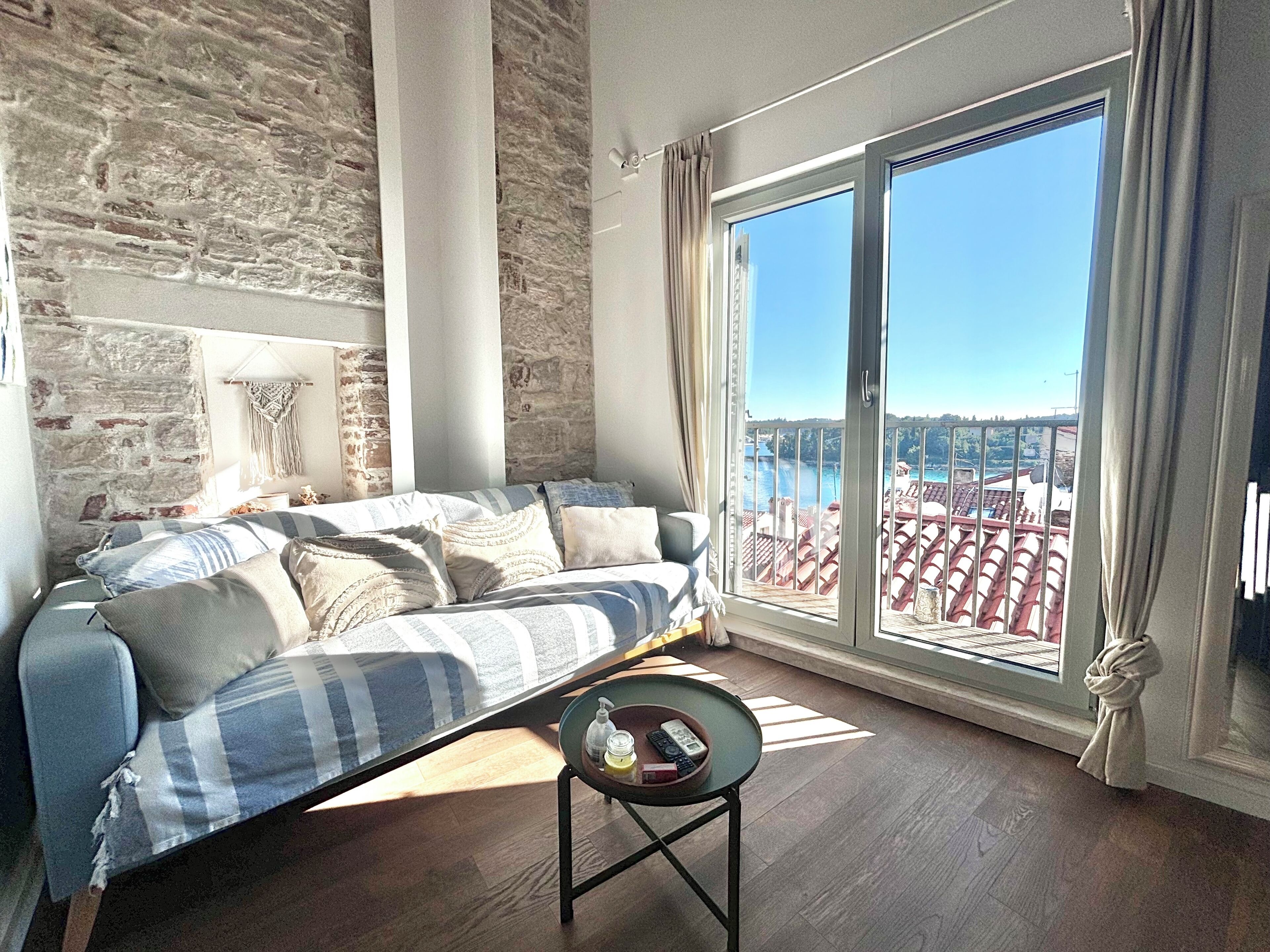 A living room with a sofa, a small table, and a view of a balcony with red tiles.