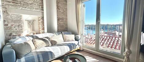 A living room with a sofa, a small table, and a view of a balcony with red tiles.