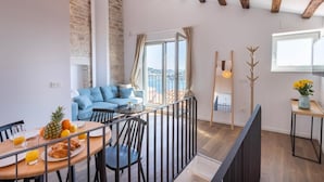 A modern living room with a balcony, wooden beams, a sofa, and a dining area with breakfast items. - Seagull's View - Breezy 1 Bedroom with Seaview in the Heart of Rovinj's Old Town (Rovinj)