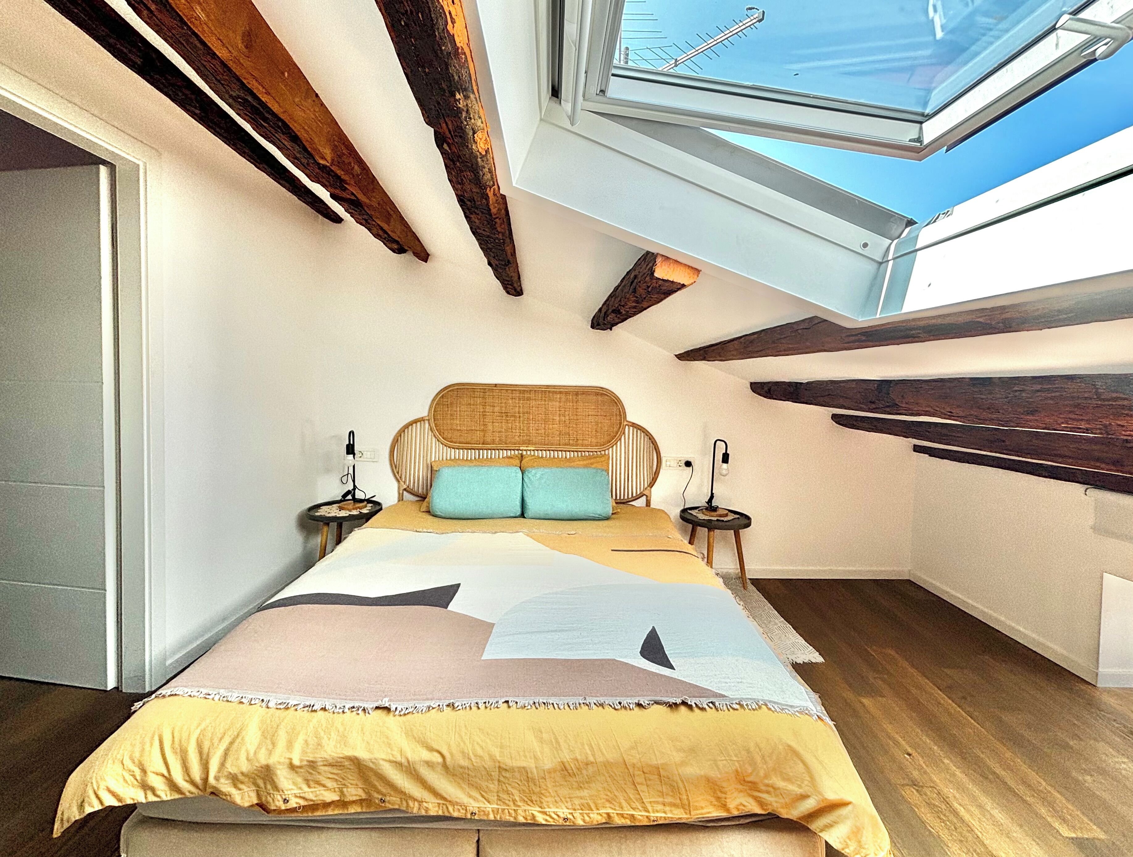 A bedroom with a bed, bedside tables, a window, and exposed wooden beams.