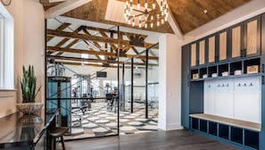 A spacious room with a high ceiling, exposed wooden beams, and a large open area with exercise equipment. There is a seating area with a bench and a potted plant.
