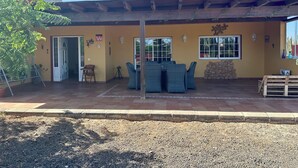 A covered patio with outdoor furniture, a stone wall, and a door leading inside. - Rustic Villa with Private Pool near Ocean, Hiking & Cycling Trails – Sleeps 9 (CN)