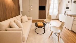 A modern living room with a sofa, chairs, a coffee table, a TV, and a kitchen area.