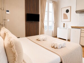 Une chambre d’hôtel avec un lit, un téléviseur fixé au mur, un petit bureau et une fenêtre avec des rideaux.