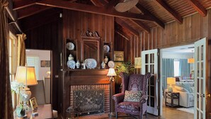 A cozy living room with a fireplace, wooden beams, and a large armchair.