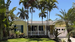 A yellow house with a white porch, surrounded by palm trees and a well-maintained lawn.
