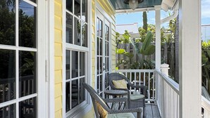 A wooden porch with two wicker chairs and a table, yellow siding, and a blue ceiling.