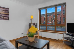 A modern living room with a large window, a sofa, a table with a plant, and a TV.