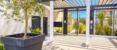 A modern building entrance with a covered walkway, a large planter with a tree, and a view of the surrounding area.