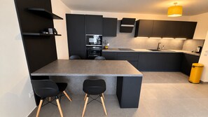 Una cocina moderna con encimera gris, sillas negras y muebles oscuros.