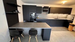 A modern kitchen with dark cabinetry, a central island with stools, and a built-in oven. - Charming 3 rooms located in Le Cannet, near Cannes (Le Cannet)