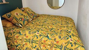 A bedroom with a floral-patterned bedspread, a round mirror, and a small shelf with decorative items. - Apartment near the royal square, Nantes (Nantes)