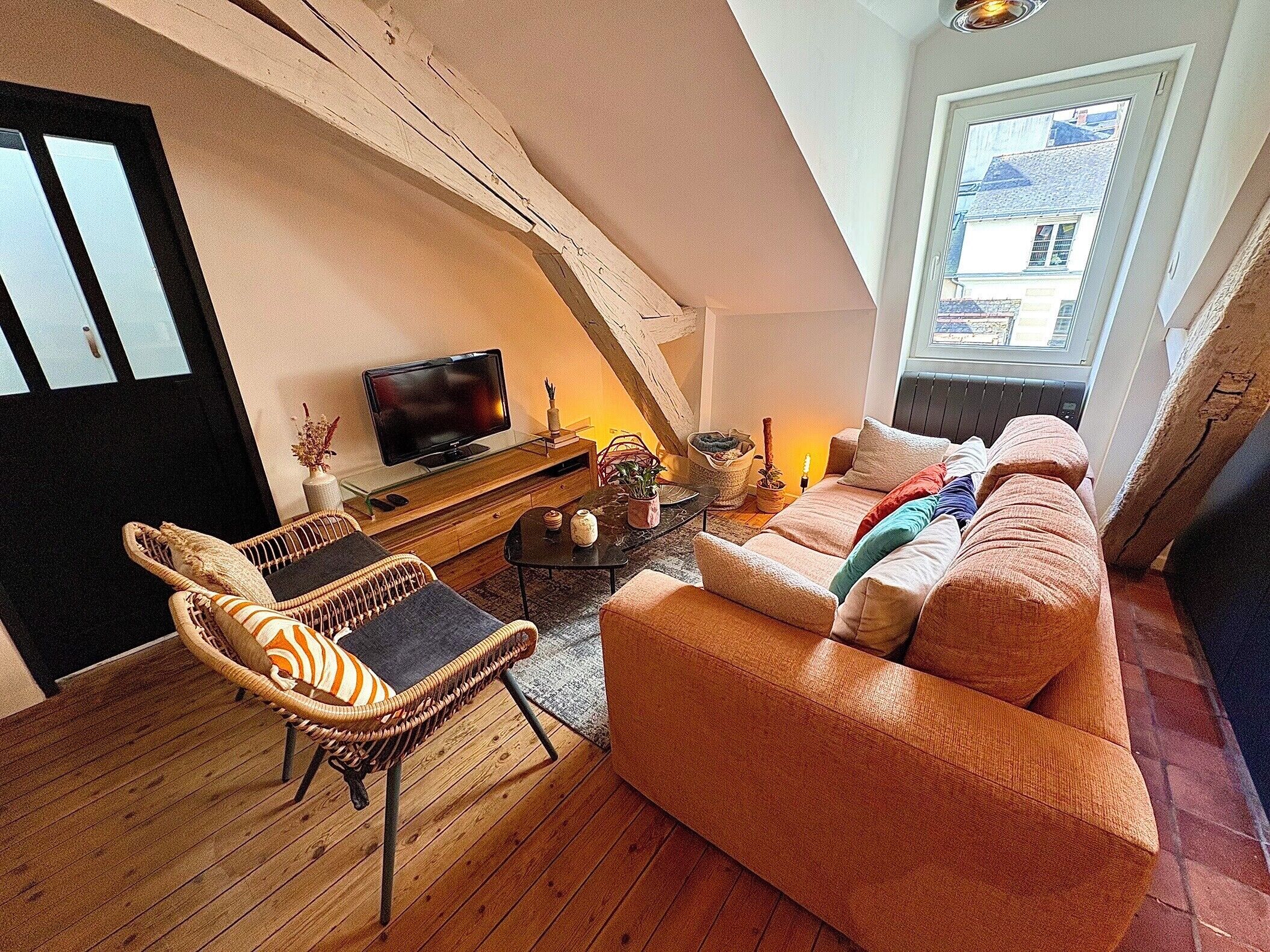 A cozy loft-style living room with a television, wicker furniture, and a large window.