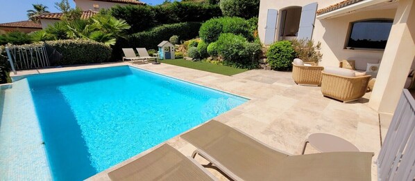 A swimming pool with lounge chairs, a small playhouse, and a patio area with wicker furniture.