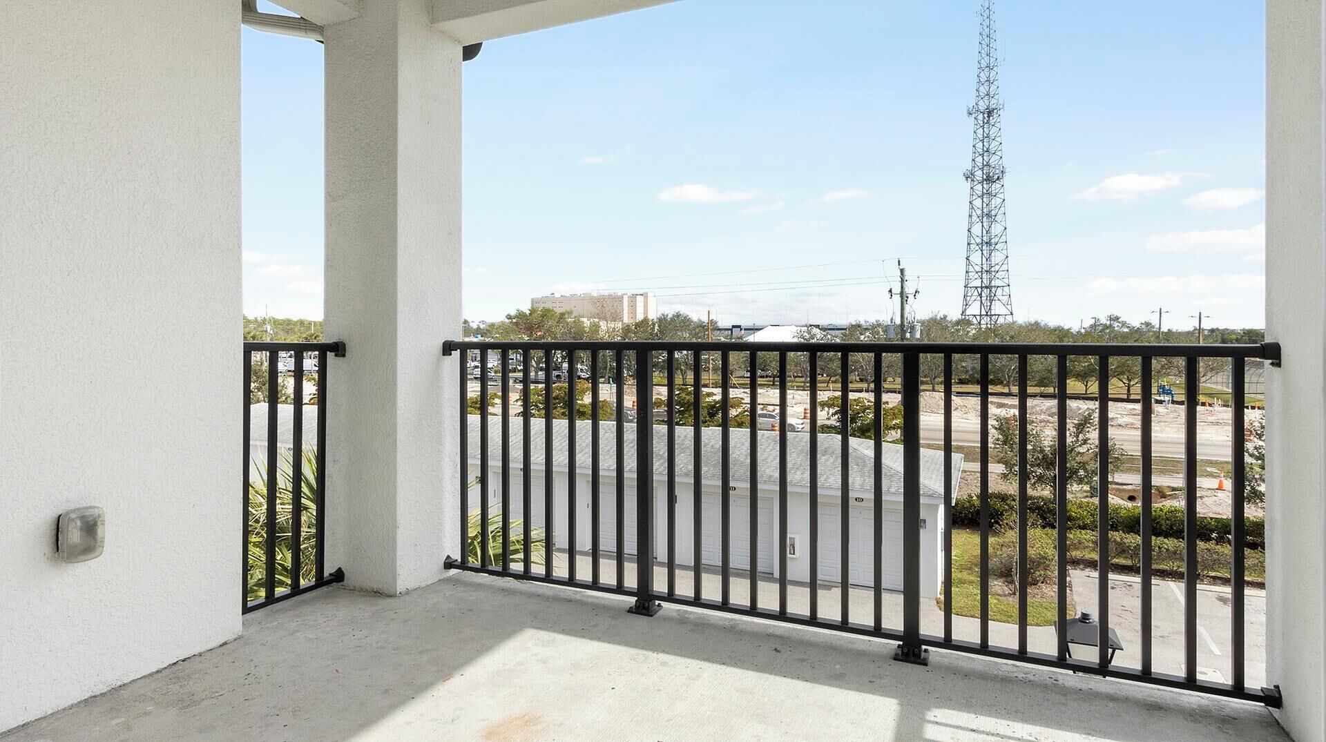 Un balcon doté d’une balustrade en métal, donnant sur un parking et sur un pylône d’une ligne électrique éloignée.
