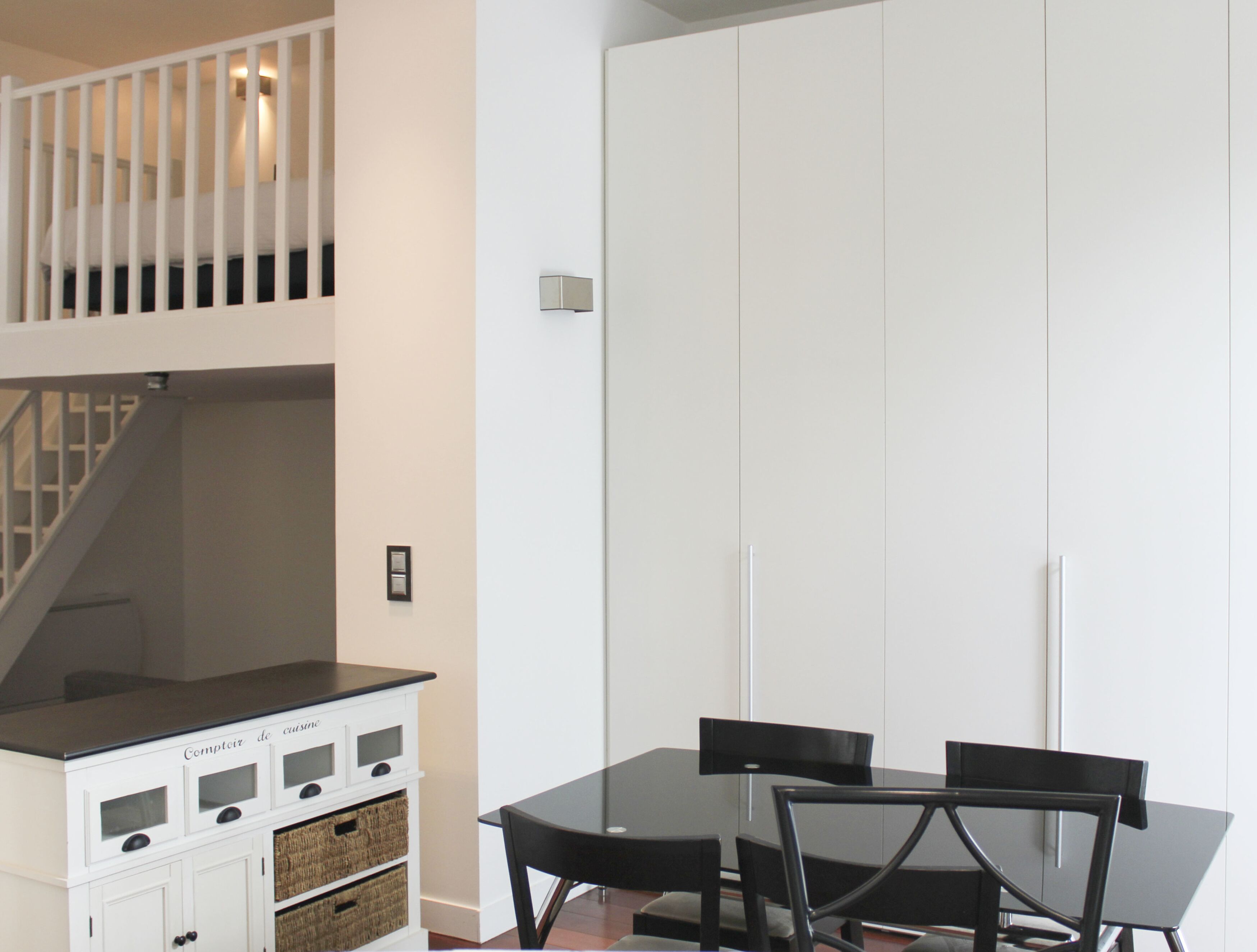A dining area with a black table and chairs, a white cabinet with baskets, and a white wardrobe.
