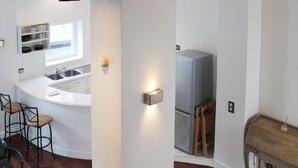 A modern kitchen with a white countertop, stainless steel sink, and a built-in refrigerator. There are bar stools and a wooden table. - Bright apartment with mezzanine in Asnières (Asnières-sur-Seine)