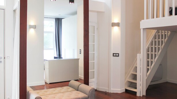 A modern interior with a wooden floor, a white staircase, and a seating area with a cushioned bench. - Bright apartment with mezzanine in Asnières (Asnières-sur-Seine)