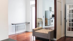 A modern apartment with hardwood floors, a grey sofa, a small table, and a kitchen area with a washing machine. - Bright apartment with mezzanine in Asnières (Asnières-sur-Seine)