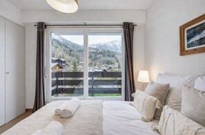 Een slaapkamer met een bed, een raam met gordijnen, een lamp en een lijst met een foto aan de muur.