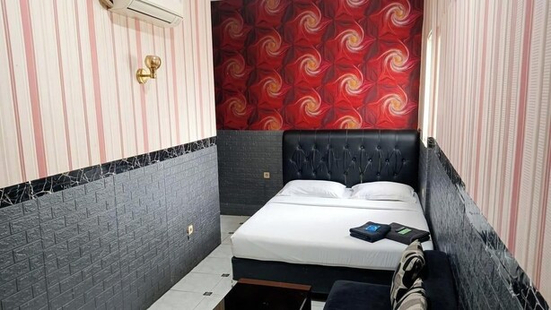 Ein schmales Hotelzimmer mit einem Bett, einer Bank und einer Wand mit Muster.