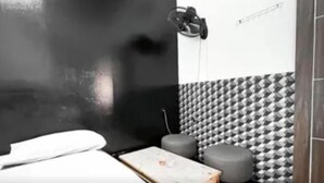 Un baño con lavamanos blanco, un espejo, una toalla, un taburete pequeño y un papel tapiz estampado.