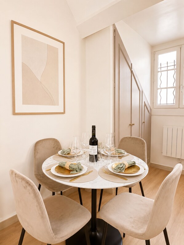 A dining area with a round table, four chairs, a bottle of wine, and empty wine glasses. - 2066 Princesse (Paris)