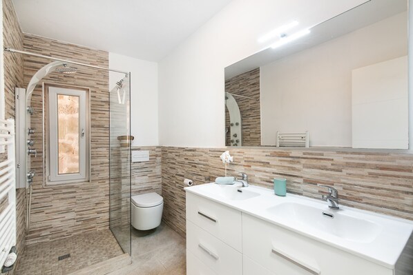 A modern bathroom with a glass-enclosed shower, a white sink with a mirror, and a tiled wall.