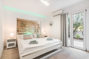 A modern bedroom with a large bed, a stone accent wall, a round mirror, and a view through a glass door.