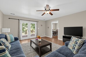 A living room with a ceiling fan, a TV, a coffee table with a vase, and a sofa with patterned cushions.