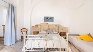 Un dormitorio con cama, mesita de noche, sillón, sofá y una obra de arte colgada en la pared.