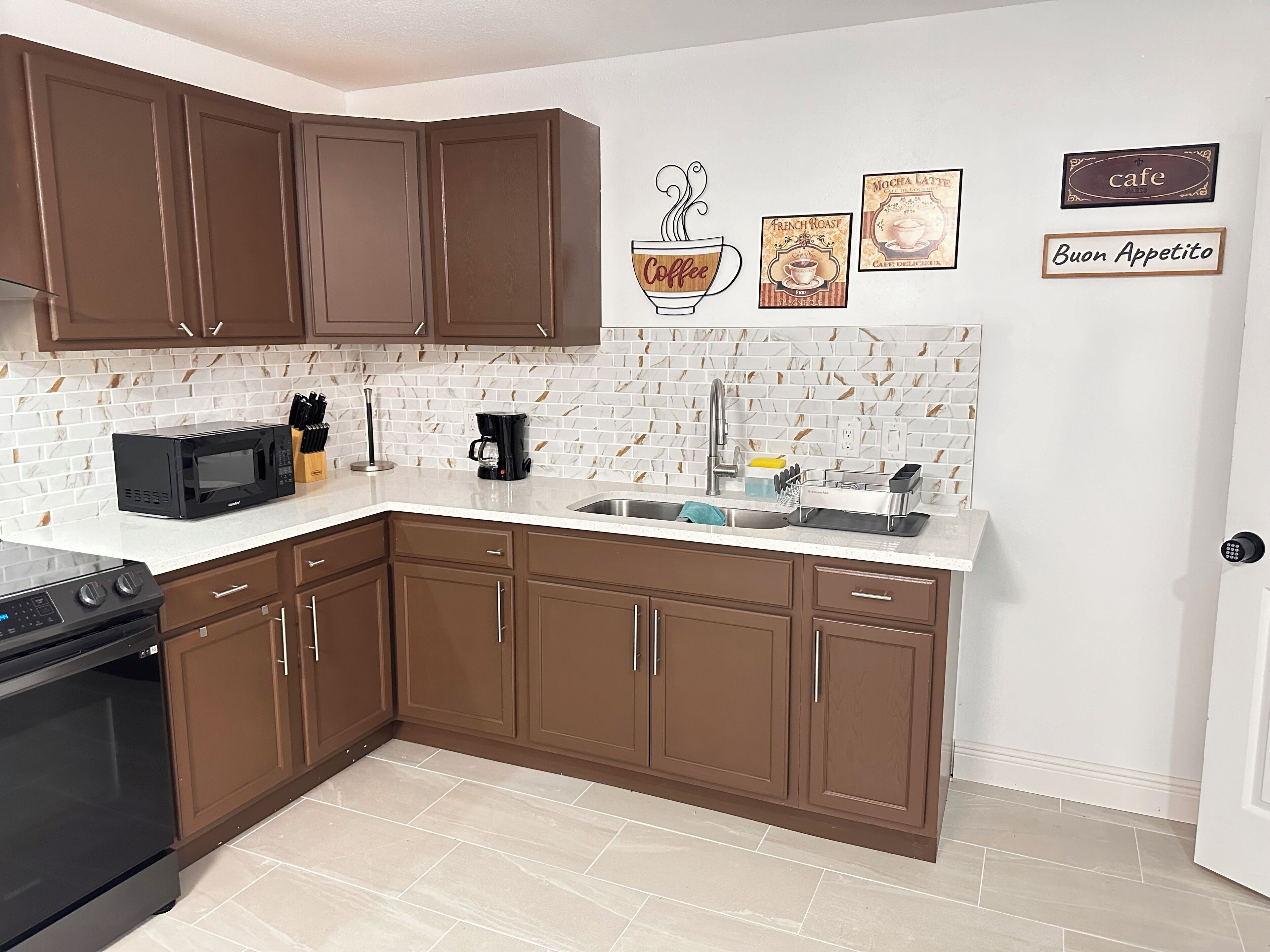A kitchen with brown cabinets, a white tiled backsplash, a coffee maker, a microwave, and a sink.