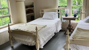 A bedroom with a large bed, a bedside table with lamps, a bookshelf, and a window with a view of greenery. - Mountain cottage. 4-bdrm cottage in the White Mountains with hiking trails. (Shelburne)