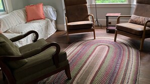 A living room with a large window, a green armchair, a brown armchair, and a patterned rug. - Mountain cottage. 4-bdrm cottage in the White Mountains with hiking trails. (Shelburne)