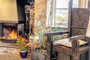 A cozy fireplace with a fire, a rustic wooden chair, and a potted plant with flowers. - 5 Bed in Littleham (oc-b30981) (Littleham)