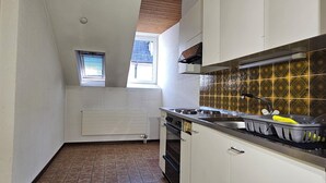 Cucina compatta con mobili bianchi, zoccolo in piastrelle e una piccola finestra.
