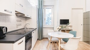 Kompakti keittiö, jossa on liesi, pesuallas ja modernit kodinkoneet. Keittiössä on ruokailutila, jossa on pöytä ja tuolit, ja televisiota varten on hylly.