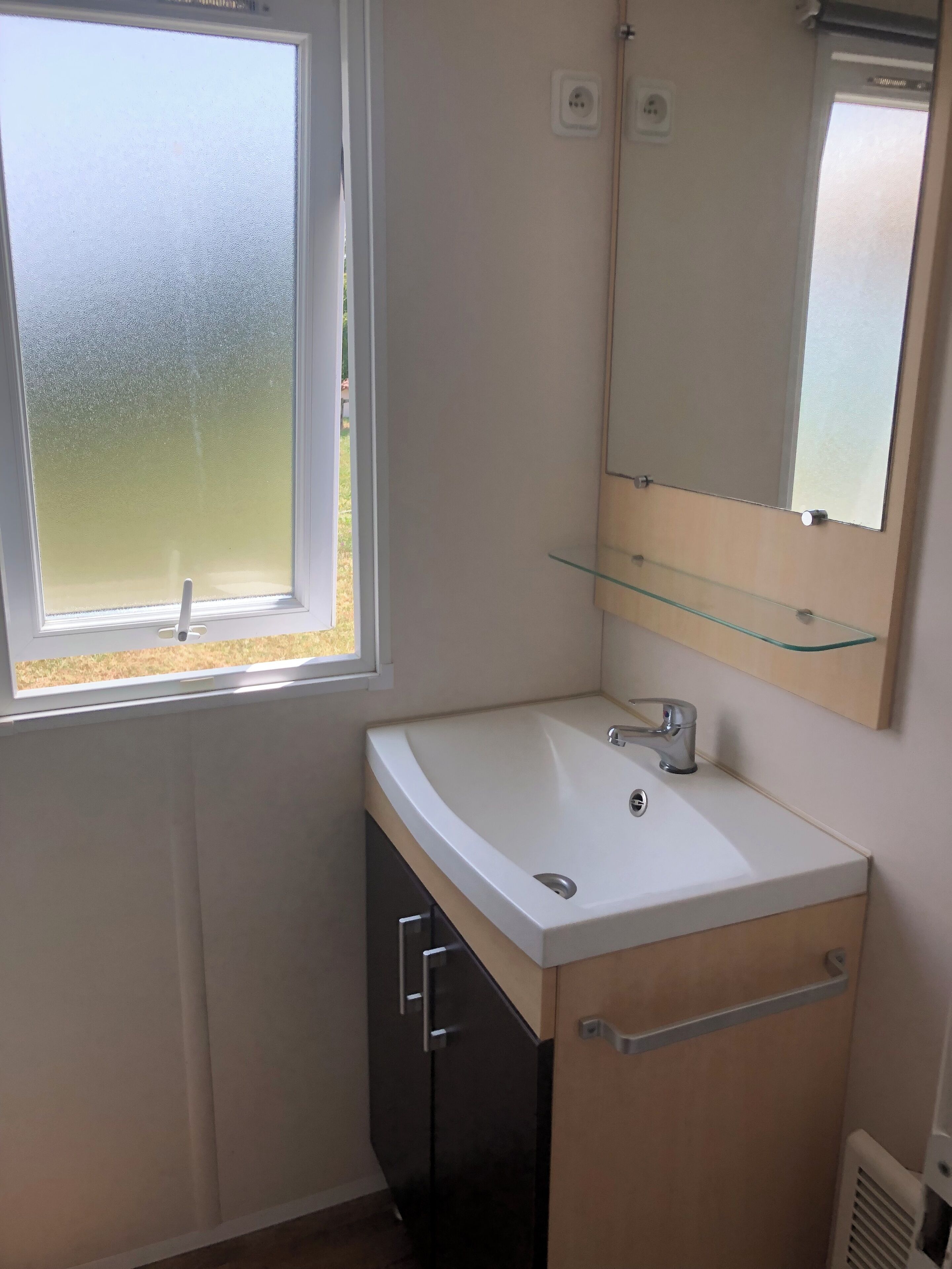 A bathroom with a white sink, a mirror, and a window.