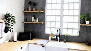 Una cocina con ventana, estantes de madera, un lavamanos y un microondas.