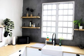 A kitchen with a window, wooden shelves, a sink, and a microwave.