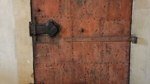 Une grande porte en bois à arc, dotée de charnières en métal et d’un cadenas.