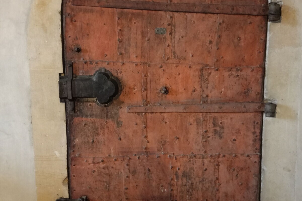 Une grande porte en bois à arc, dotée de charnières en métal et d’un cadenas.