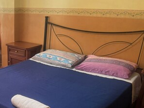 A bed with a blue bedspread, two patterned pillows, a wooden nightstand, and a decorative border on the wall. - Santa Caterina agli Acquedotti  (Rome)