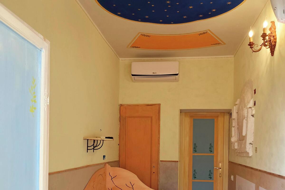 Une chambre à coucher avec un lit, une porte en bois, une armoire et un plafond décoré de motifs en forme d’étoiles.