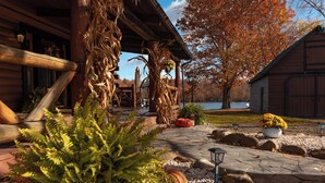 A rustic cabin with a stone pathway leading to the entrance, surrounded by autumn foliage and a lake view. - Riverfront Cabin with heated pool, Cedar wood Hot Tub, Dry Sauna, and Dock (Waterford)