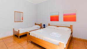 Une chambre d’hôtel avec deux lits simples, un grand lit, un miroir et deux tableaux abstraits accrochés au mur.