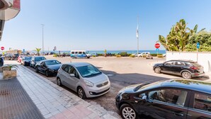 Un parking rempli de voitures, un panneau de signalisation indiquant un arrêt obligatoire et une vue sur la mer.